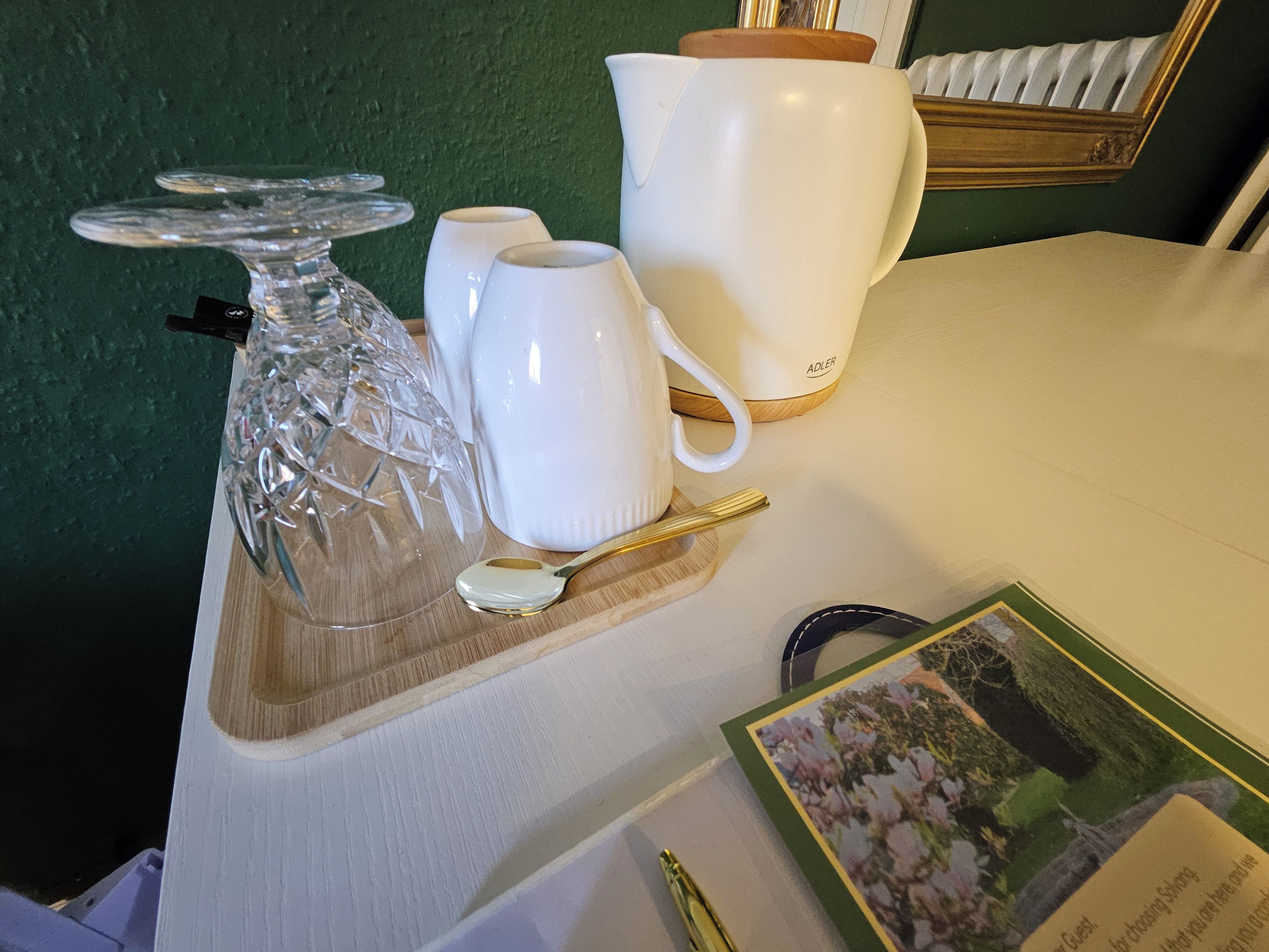 A table with a crystal decanter, white cups, a gold spoon, a white pitcher, and a framed picture.