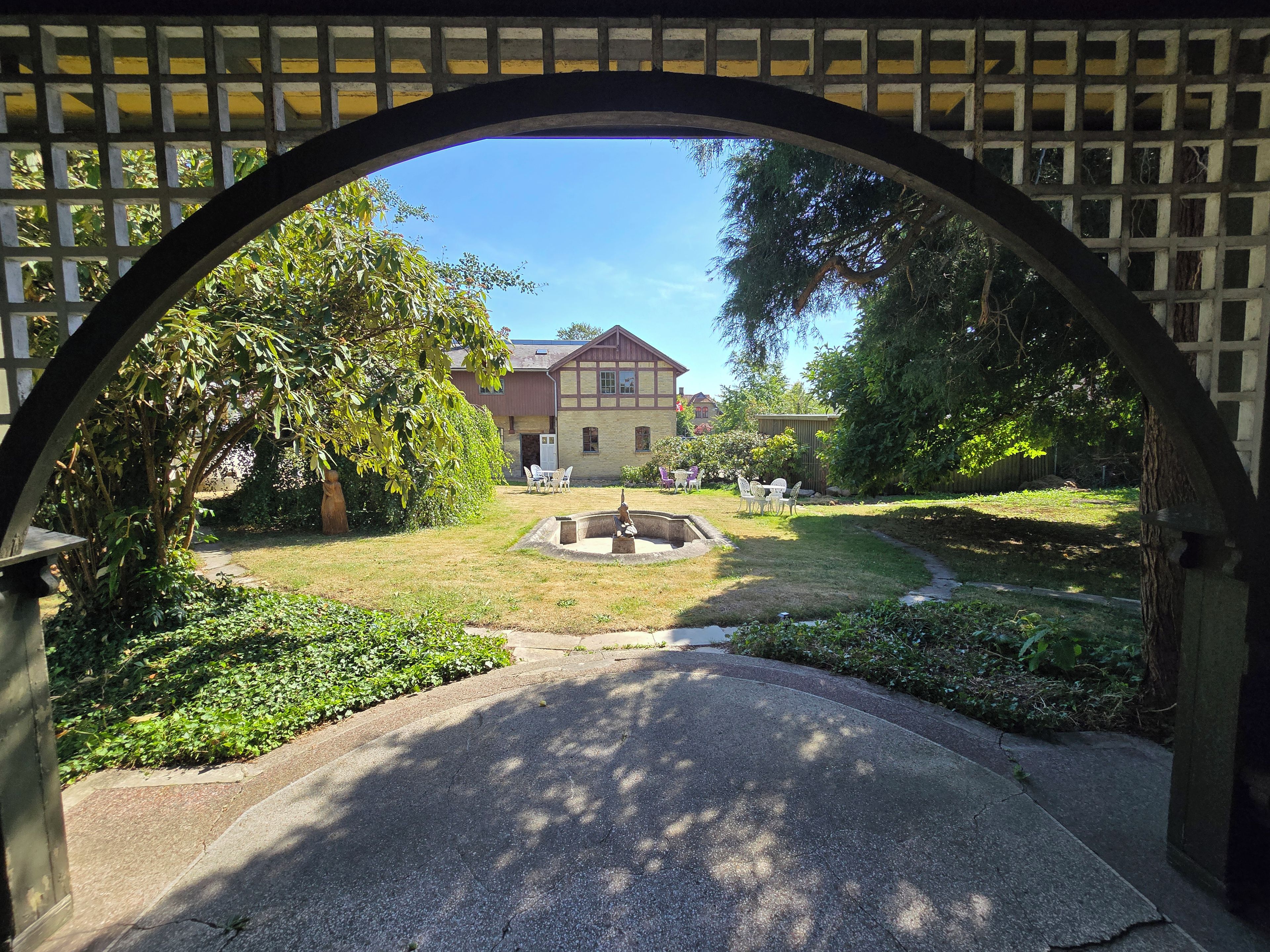 A courtyard with a fountain, surrounded by greenery and a building with a red roof.