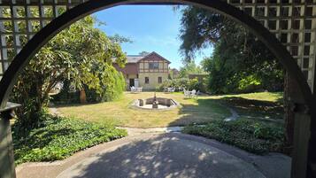 A courtyard with a fountain, surrounded by greenery and a building with a red roof.