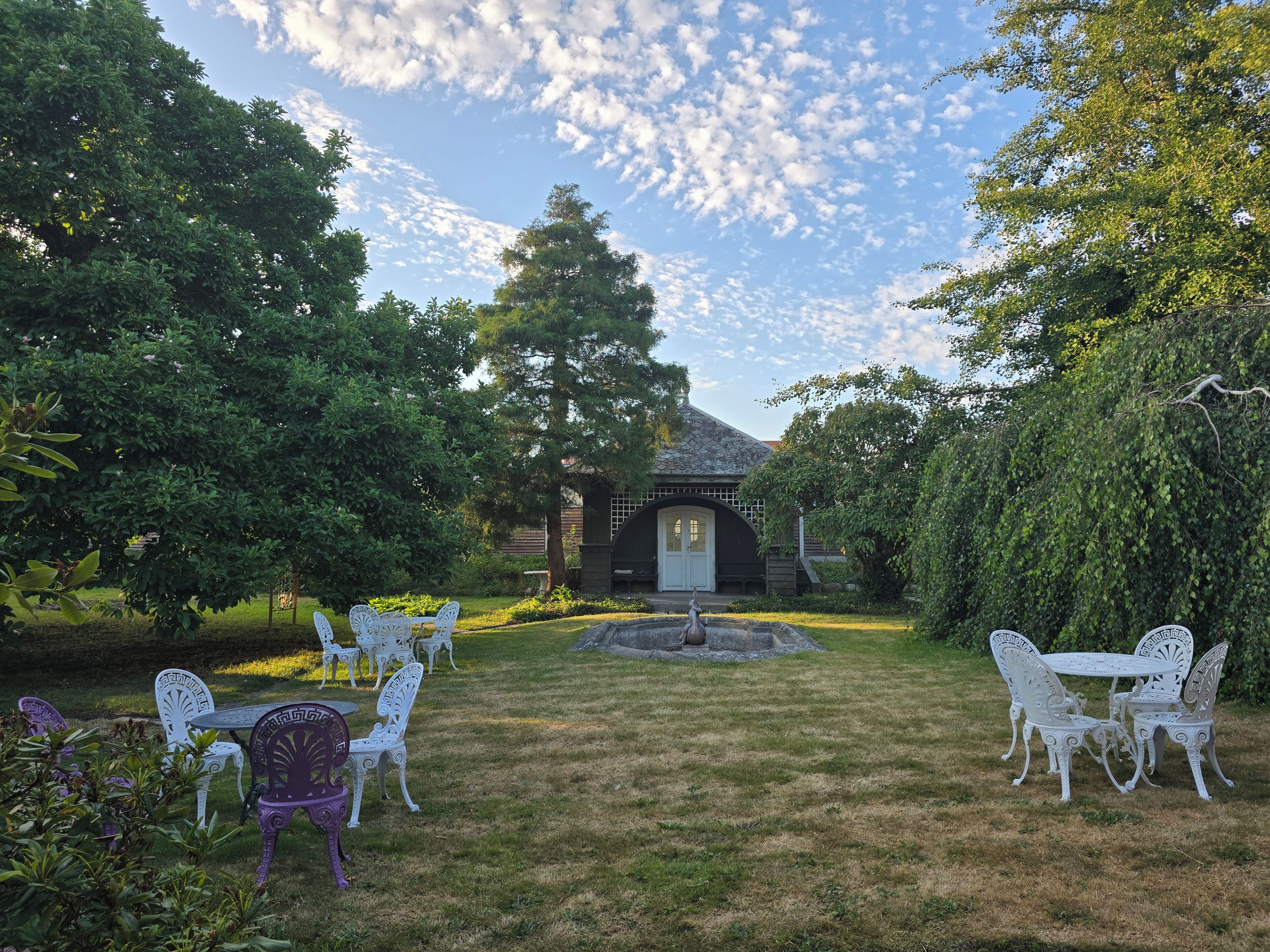 A garden with a gazebo, white and purple outdoor furniture, and a fountain.