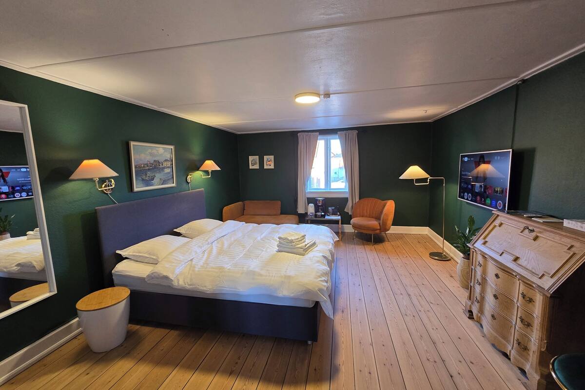 A hotel room with a bed, a chair, a dresser, a mirror, and a television.