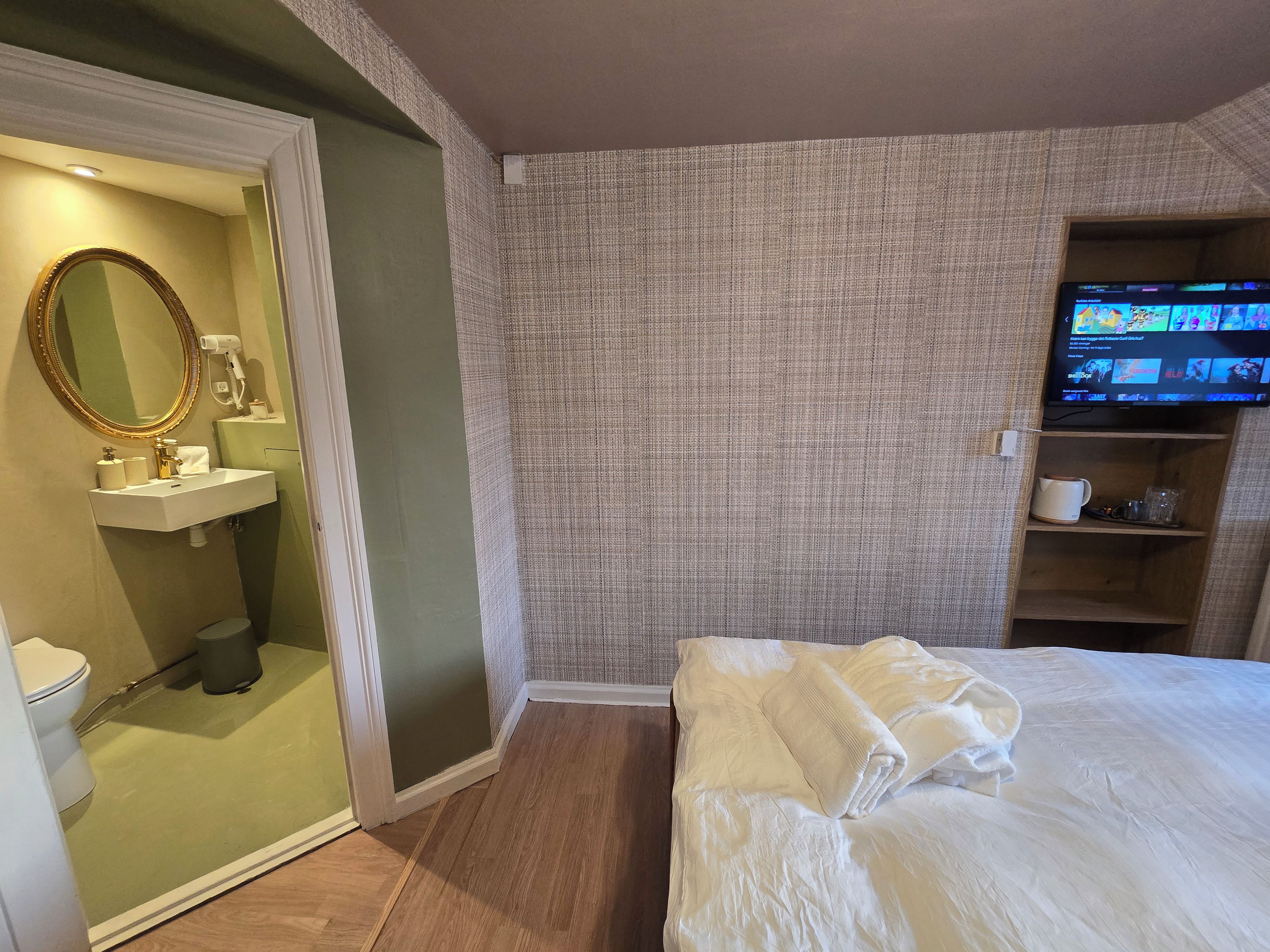 Una camera d'albergo con un letto, una televisione, un bagno con uno specchio e uno scaffale con degli oggetti.