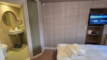 Una camera d'albergo con un letto, una televisione, un bagno con uno specchio e uno scaffale con degli oggetti.