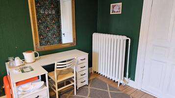 A room with a white desk, a chair, a radiator, and a mirror on the wall.