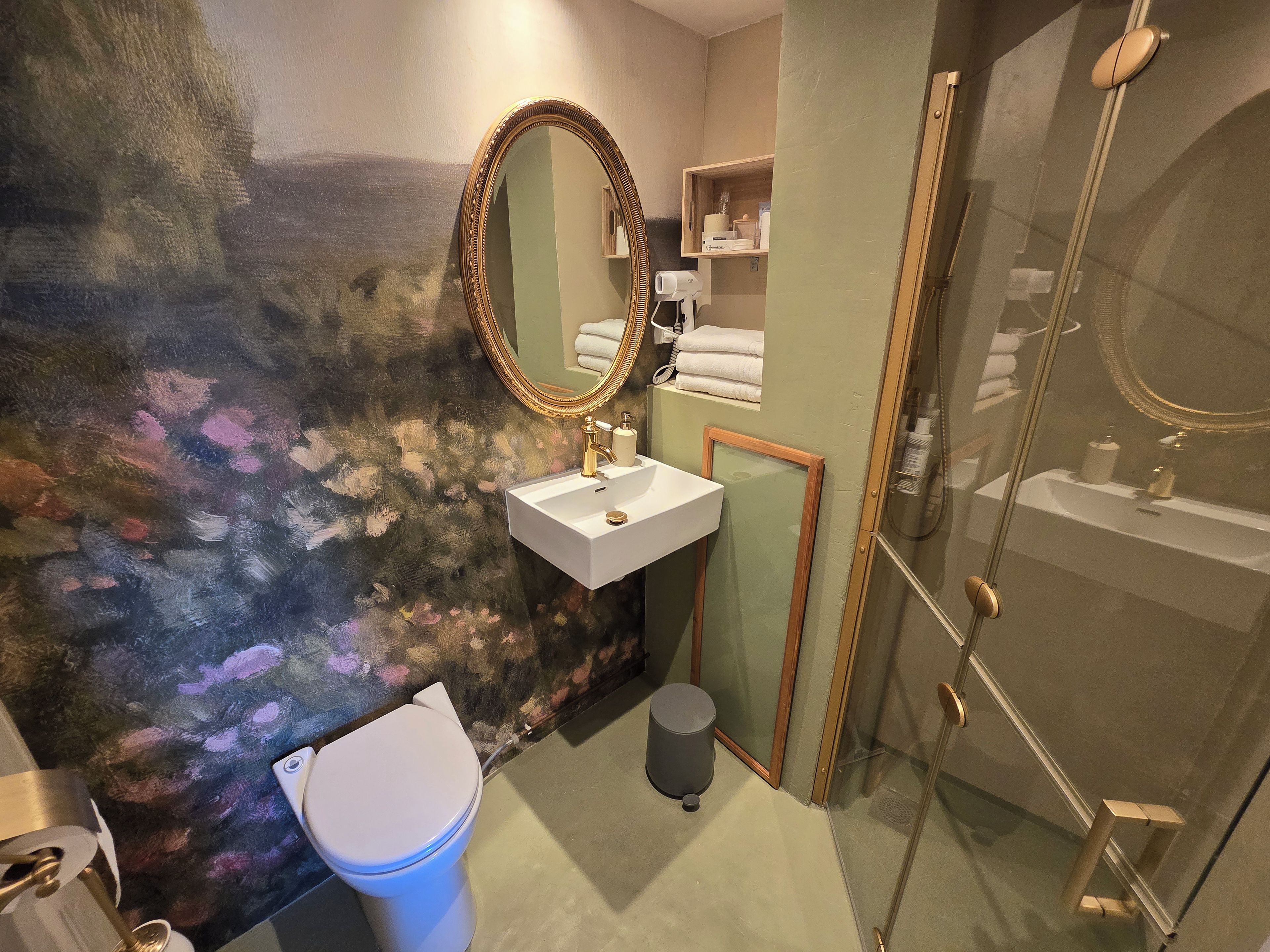 A bathroom with a white sink, a gold-framed mirror, a toilet, and a shower area.