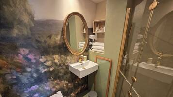 Un baño con un lavamanos blanco, un espejo con marco dorado, un inodoro y una zona de ducha.