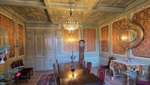A formal dining room with a large table, chairs, a chandelier, and a clock on the wall.