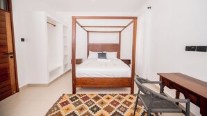 Ein Schlafzimmer mit Himmelbett, einem Holztisch, einem Stuhl und einem gemusterten Teppich.