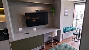 Una cuina moderna amb televisió integrada, una petita zona de seients amb un banc amb amortidor i un tamboret, i vista a la ciutat a través d'una finestra gran.