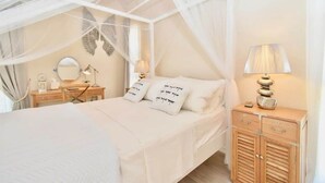 Een slaapkamer met een hemelbed, bedlampen, een dressoir en een spiegel.