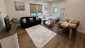 Ett kompakt bostadsutrymme med en soffa, en säng, ett matbord och ett litet köksutrymme.