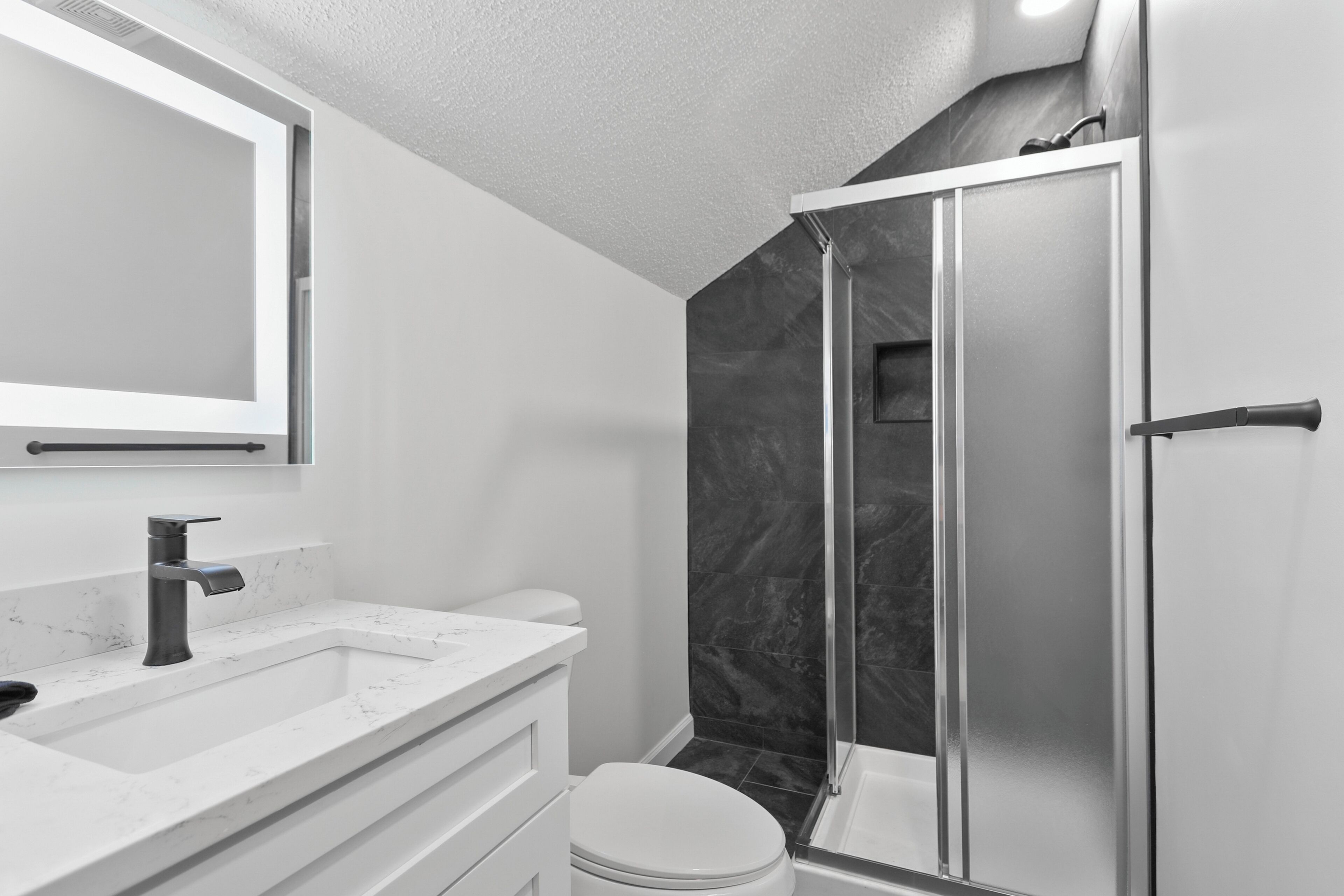 A modern bathroom with a white sink, a mirror, a toilet, and a glass shower enclosure.