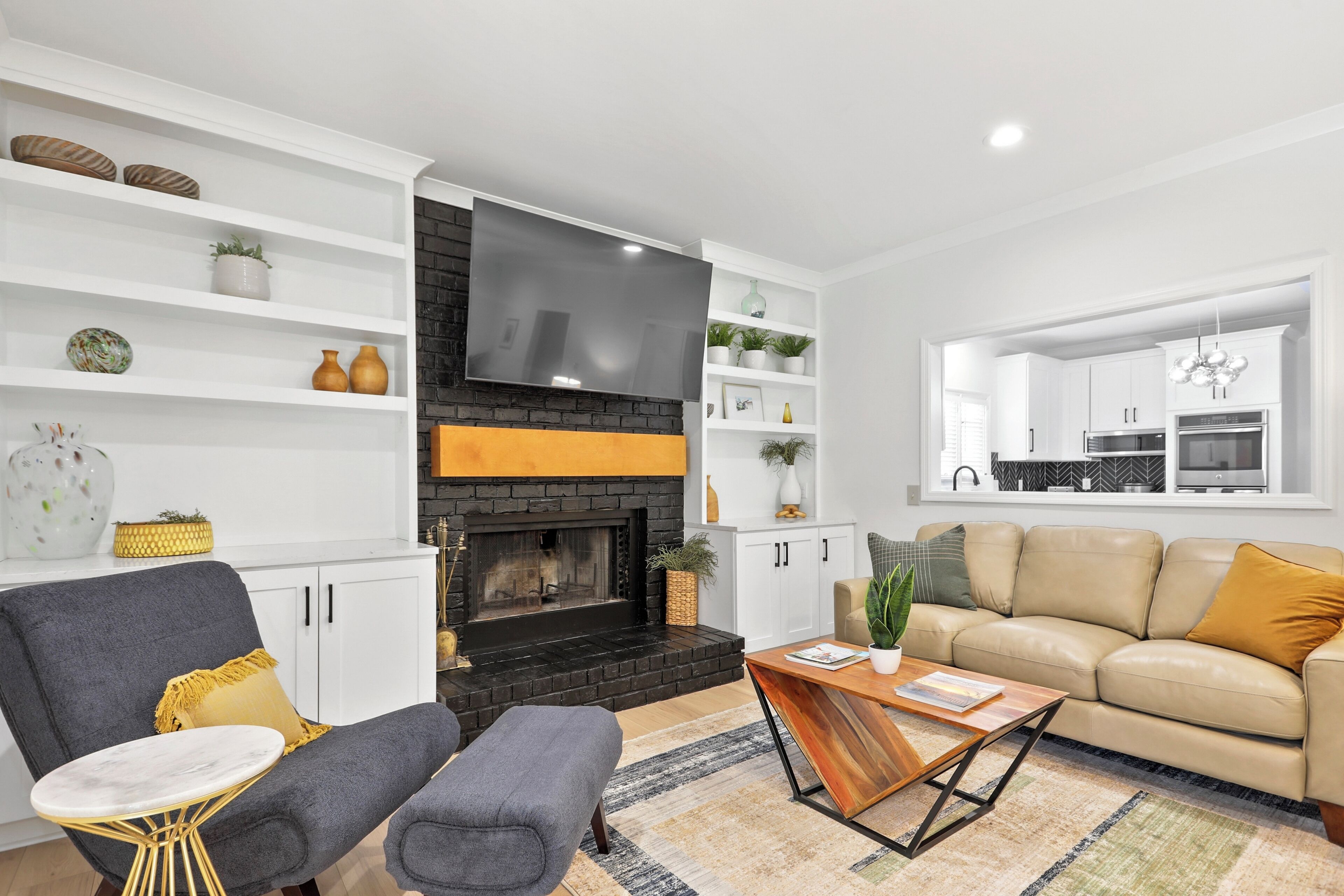 A modern living room with a fireplace, a flat-screen TV, a sofa, a coffee table, and a kitchen area visible through an open door.