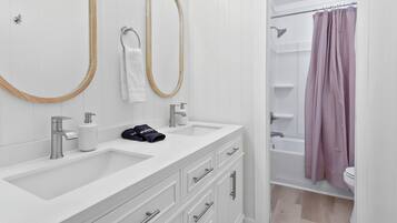 A modern bathroom with two sinks, a vanity with drawers, a large mirror, and a shower area with a pink curtain.