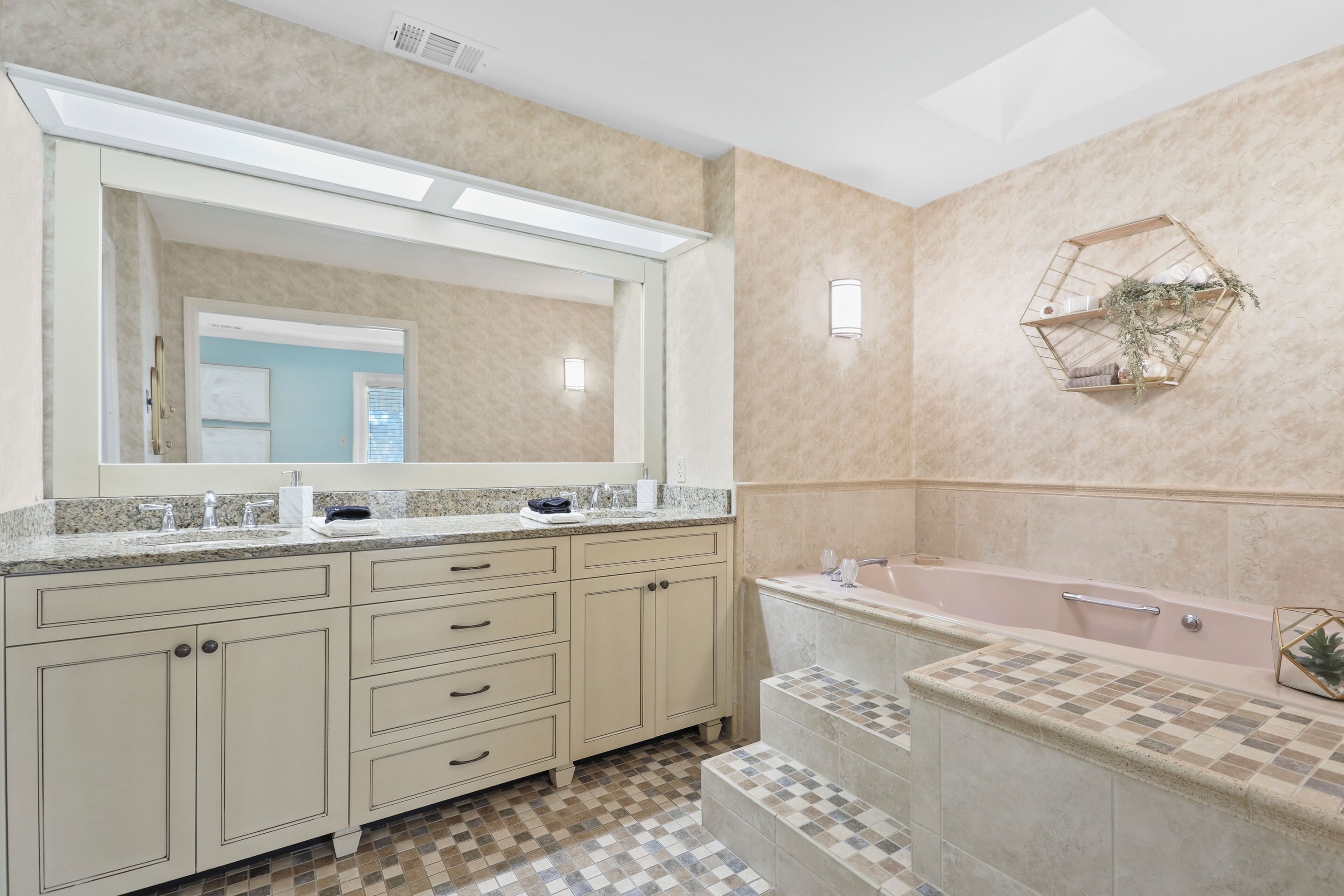 A bathroom with a large mirror, a double sink vanity, a bathtub, and a decorative wall shelf.