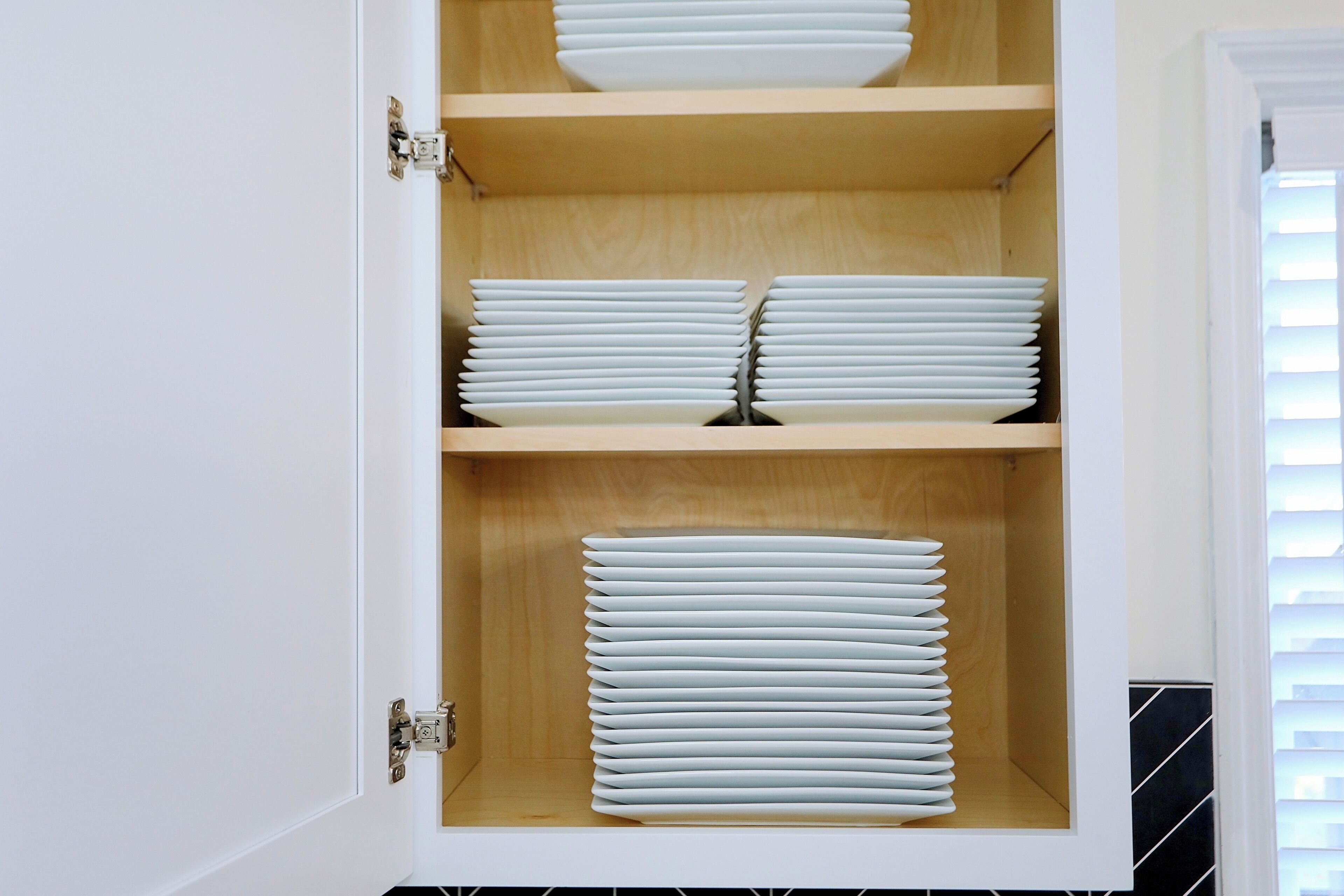 A cabinet with three shelves, each holding neatly stacked white plates.