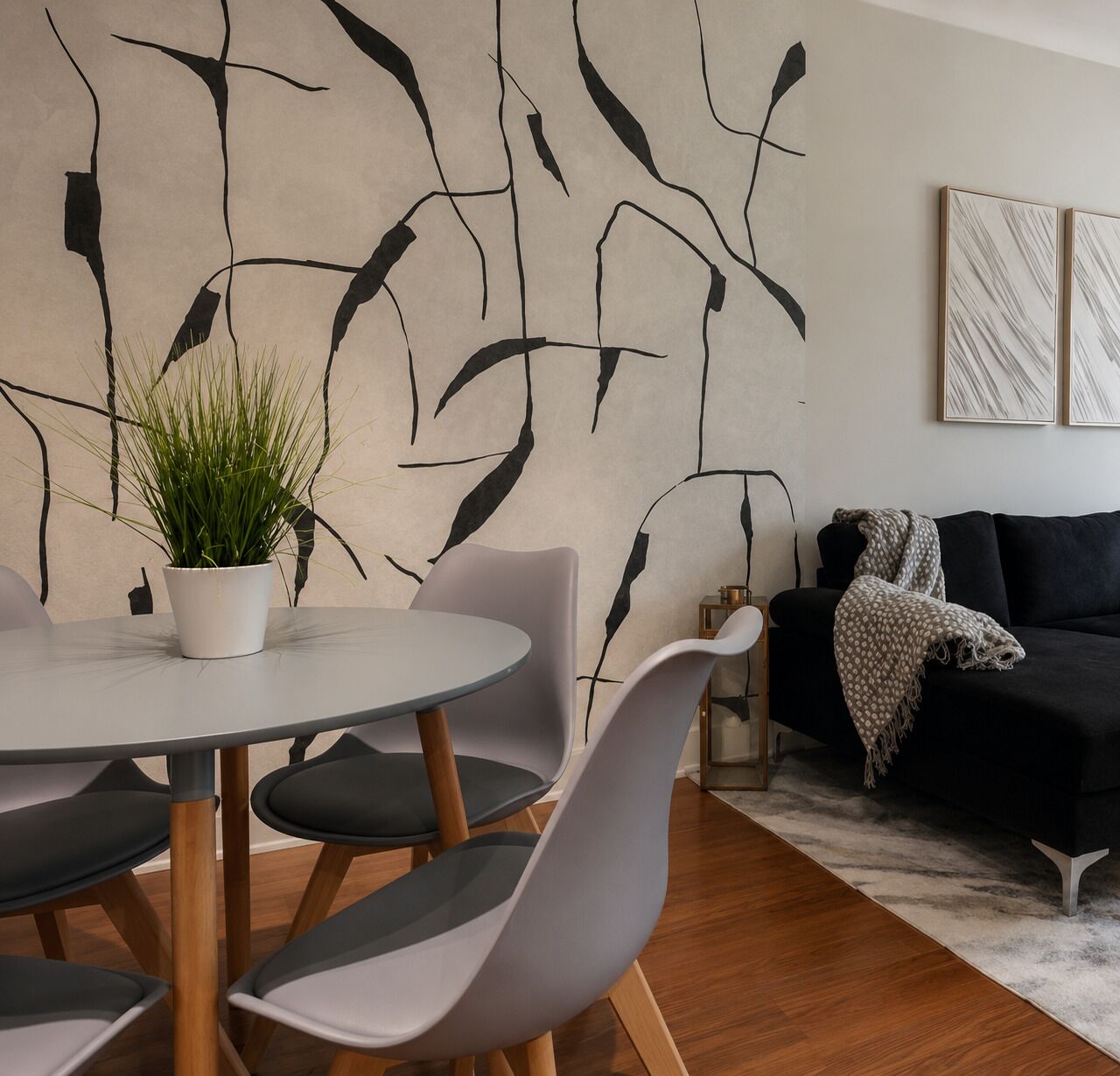 Un salon moderne avec une table ronde, des chaises grises, un canapé noir et des œuvres d’art abstraites accrochées au mur.