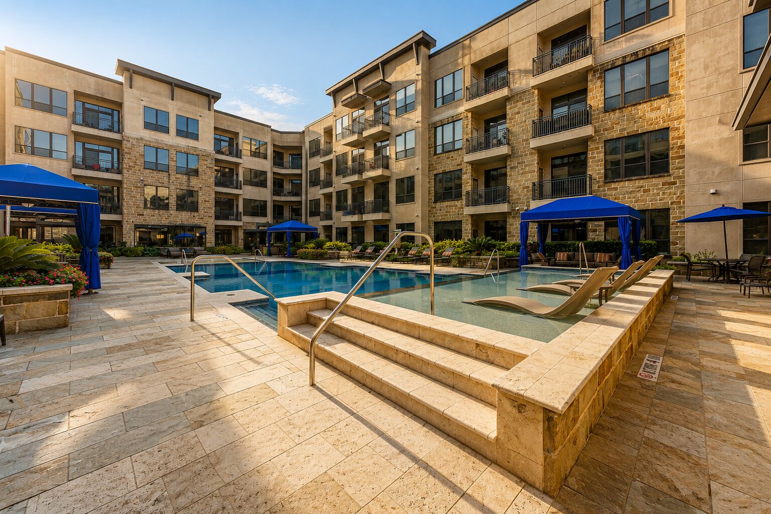 A multi-story building with a central swimming pool, outdoor seating, and blue umbrellas.