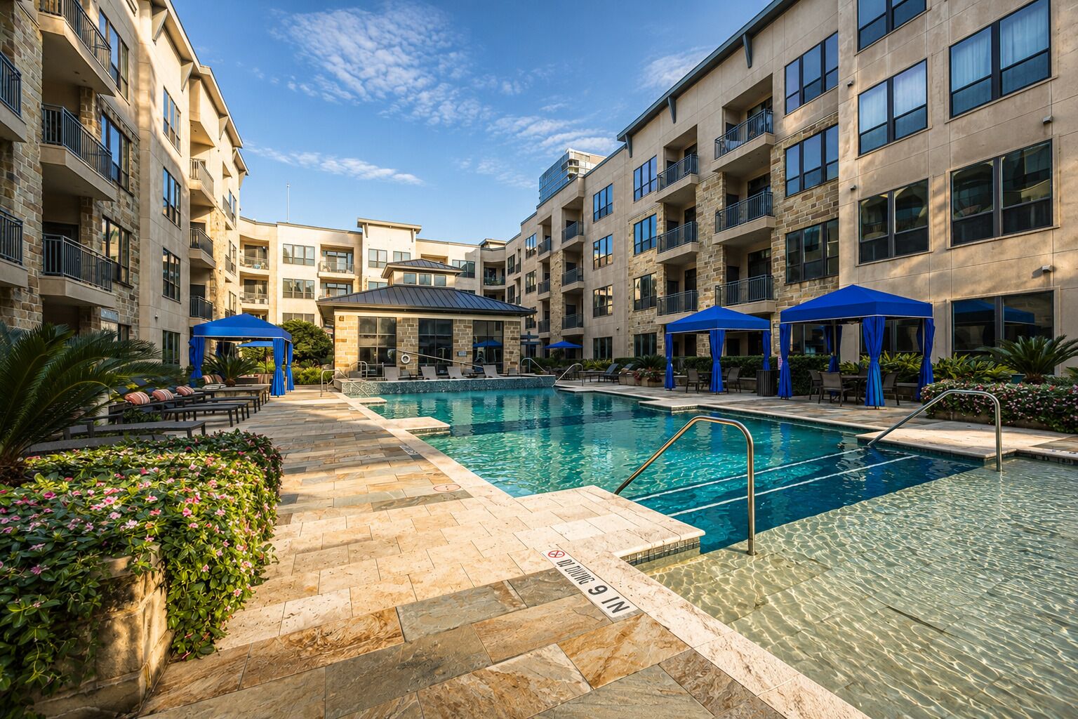 Ein mehrstöckiges Hotel mit einem zentral gelegenen Schwimmbecken, Außenbereich zum Sitzen und blauen Sonnenschirmen.