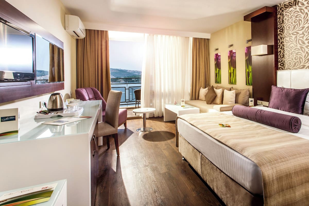 A hotel room with a bed, a desk, a chair, a small table, and a view of the outdoors.