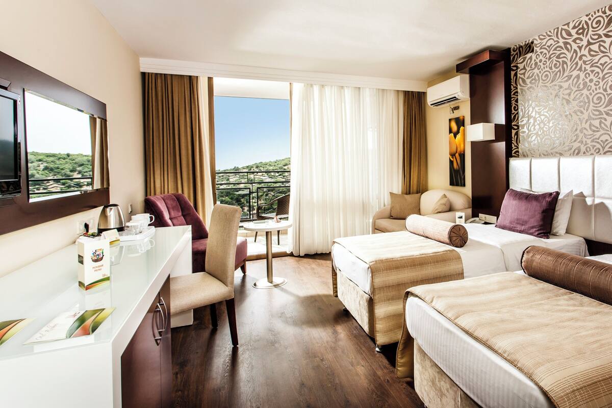 A hotel room with two beds, a desk, and a view of the outdoors.