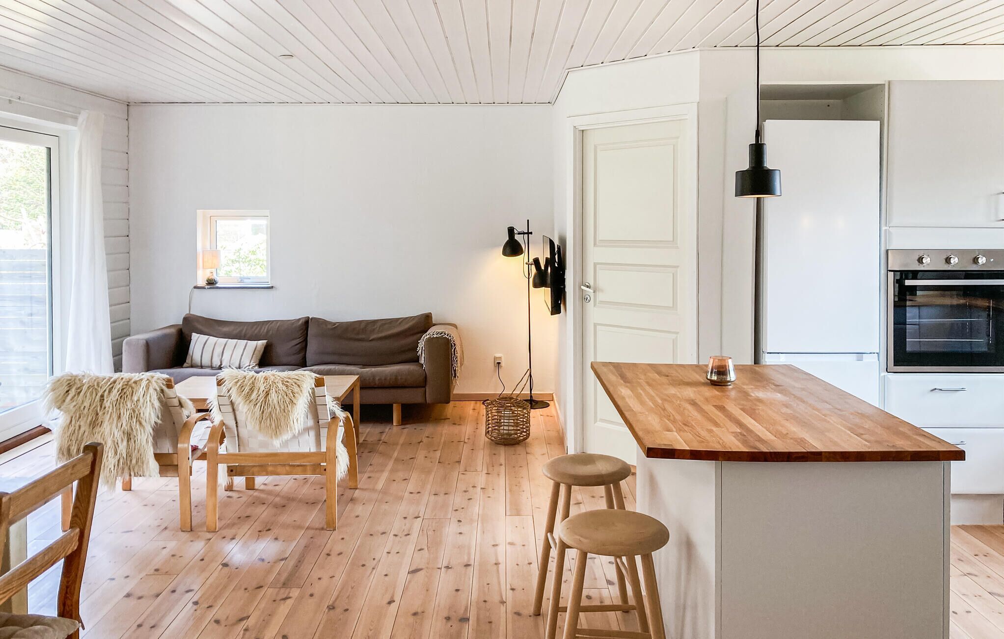 Uma cozinha moderna com uma ilha de madeira, uma área de jantar com sofá e cadeiras, e decoração em tons de branco.