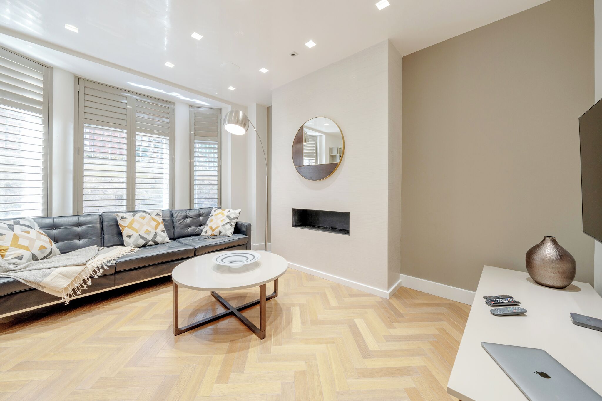 A modern living room with a sofa, a round coffee table, and a white desk with a vase and remote controls.