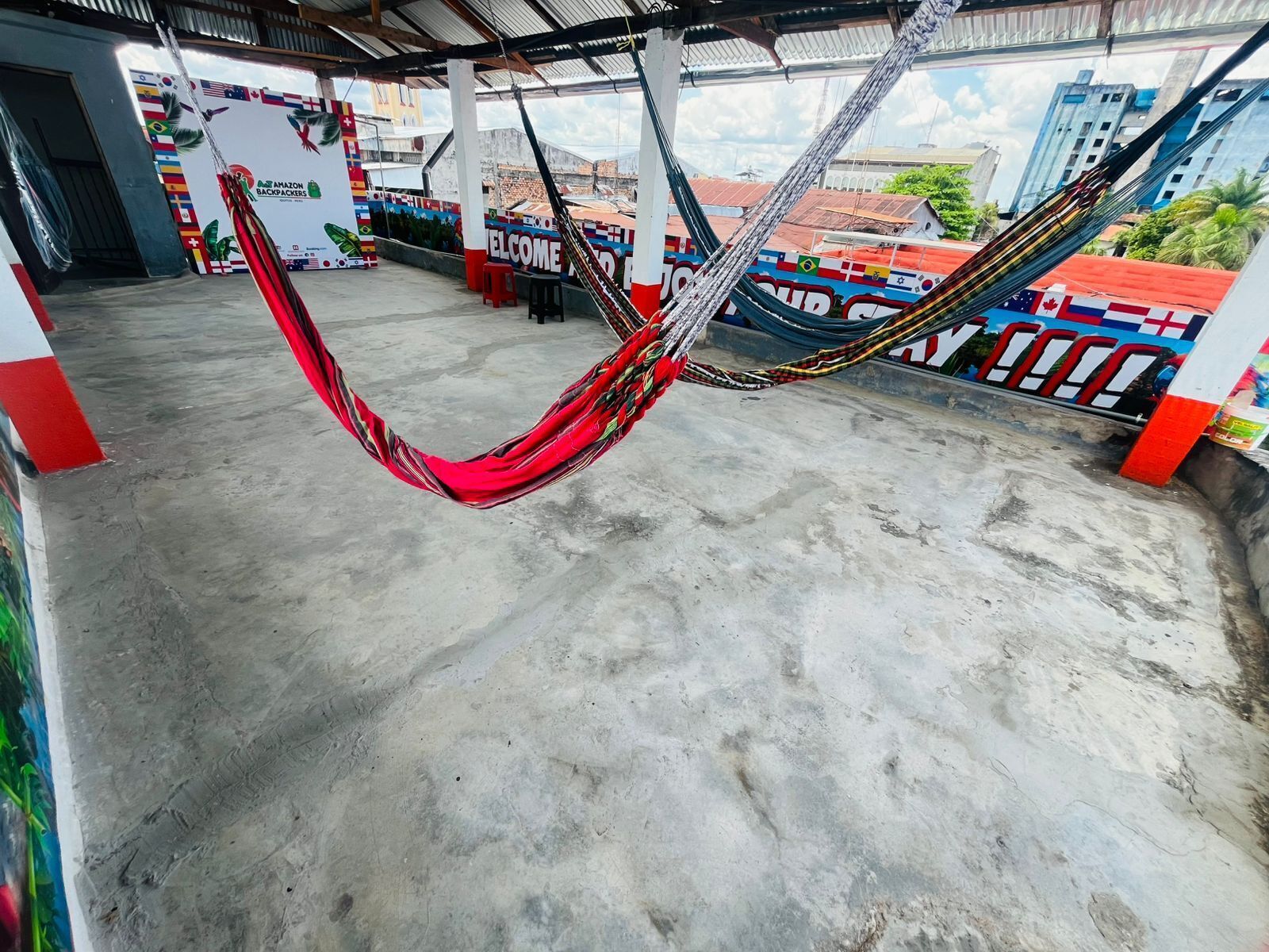 A hammock hanging in a covered outdoor area with a view of buildings and a mural with flags.