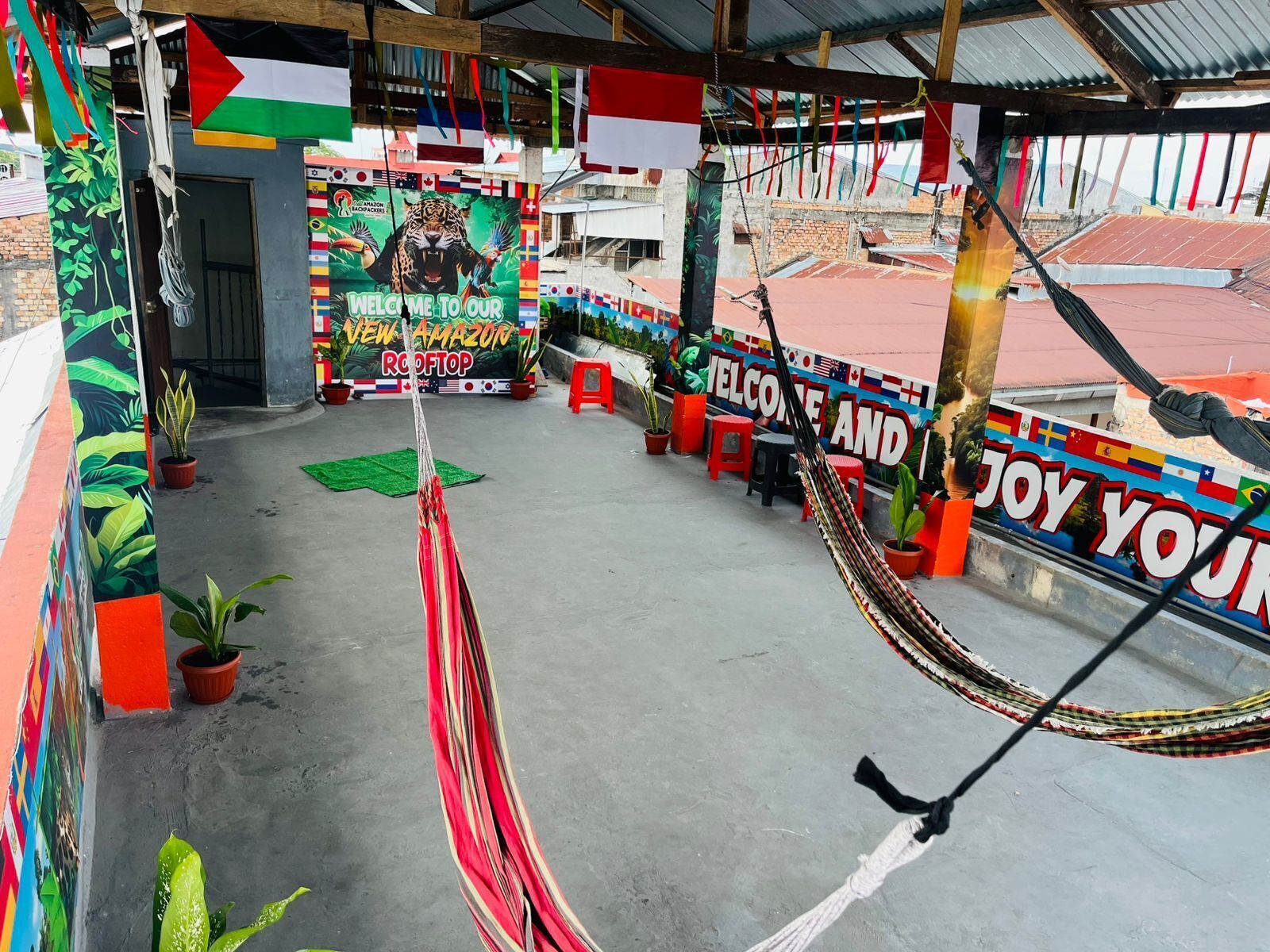 A rooftop with a hammock, potted plants, and a colorful mural with flags.