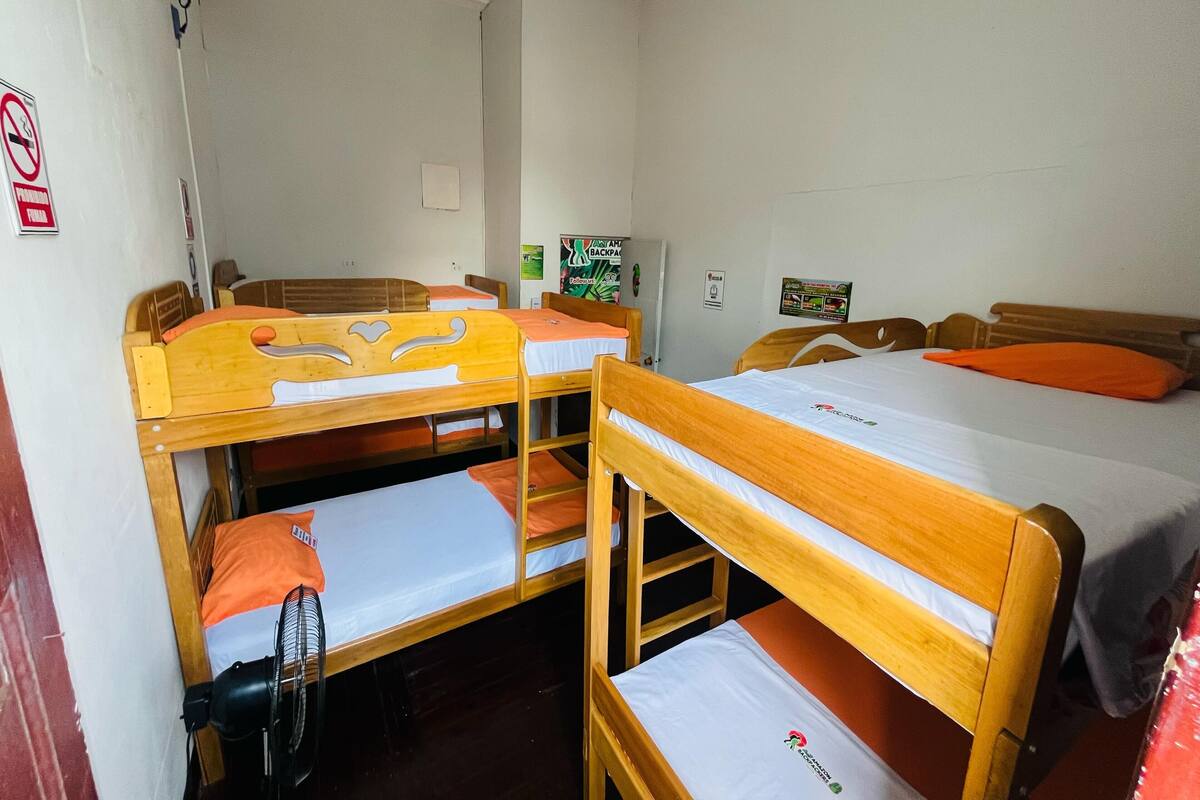 A dormitory room with bunk beds, a ceiling fan, a wall-mounted heater, and a poster on the wall.