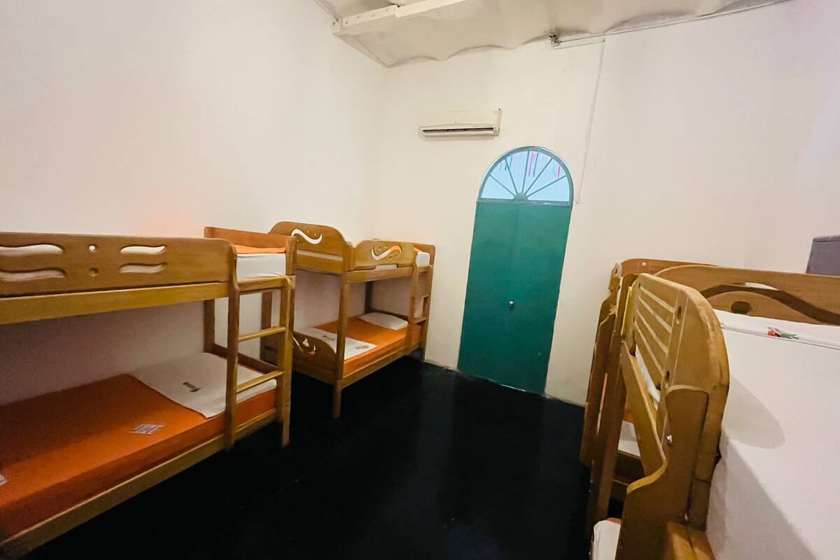A dormitory room with bunk beds, a green door, and an air conditioning unit on the wall.