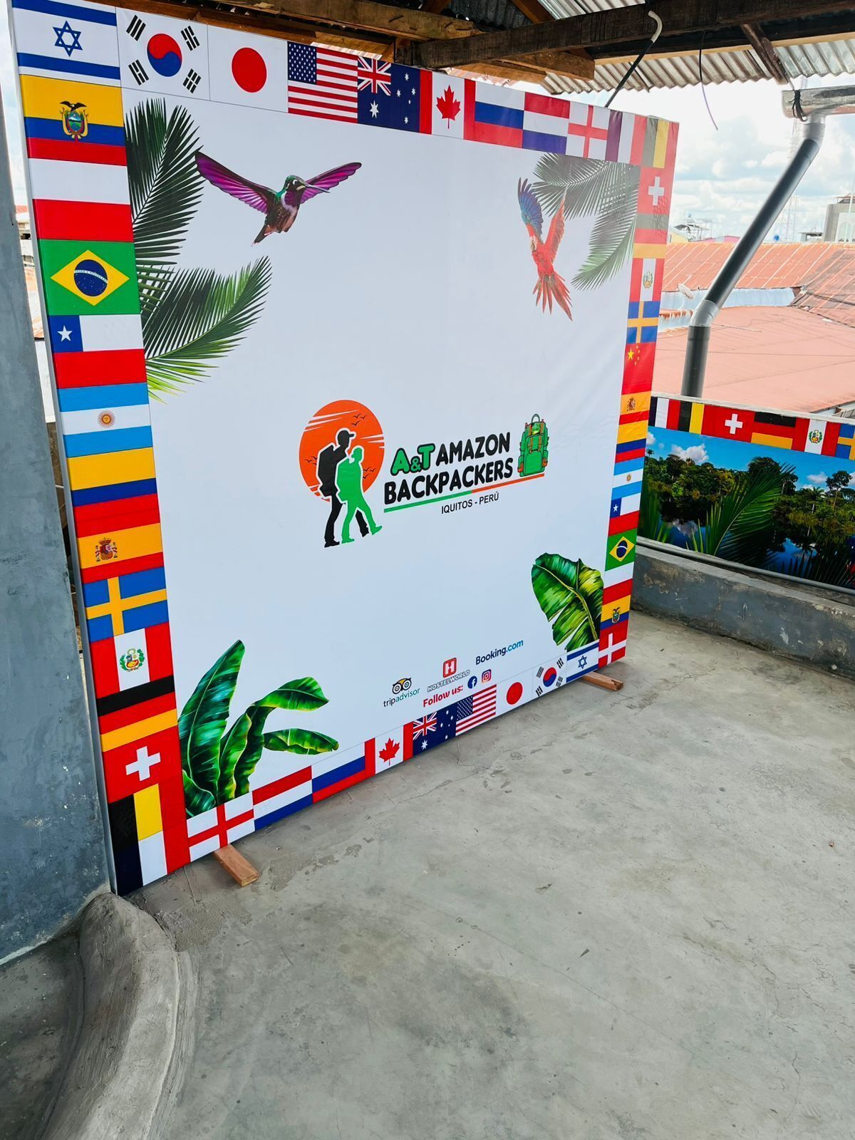 A promotional display with various national flags, a logo for A&T AMAZON BACKPACKERS, and a website address.