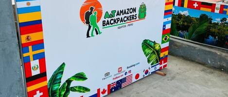 A promotional display with various national flags, a logo for A&T AMAZON BACKPACKERS, and a website address.