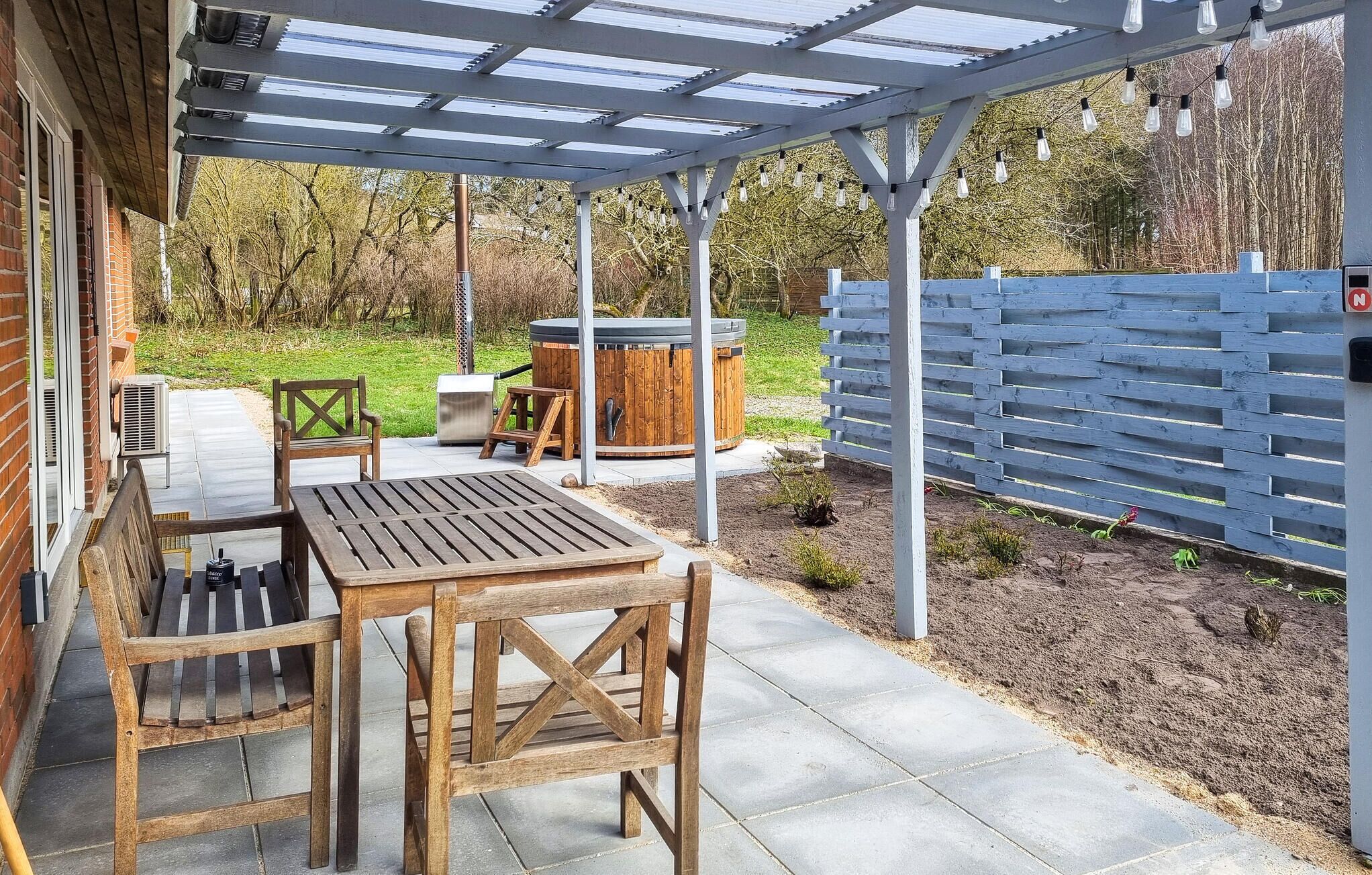 An outdoor patio with a wooden table and chairs, a hot tub, and a wooden fence.