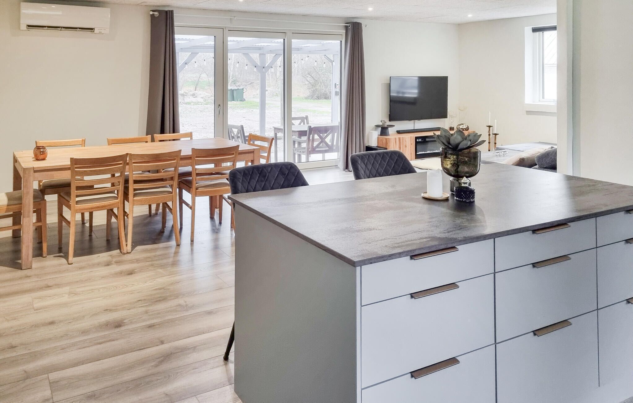 A modern kitchen with a central island, a dining area with wooden furniture, and a TV mounted on the wall.