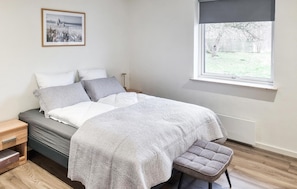 Quarto com cama, mesa de cabeceira, banco, janela e um quadro na parede.