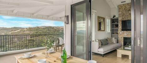 A balcony with a table set for two, a sofa, and a stone fireplace.