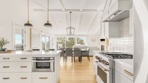 A modern kitchen with white cabinetry, a built-in oven, a gas stove, pendant lights, and a dining area with a view. - Vineyard Views w/ Pool & Game Room Near Trails, Wineries Beginnings Ranch & Vineyard by Avantstay (Paso Robles)