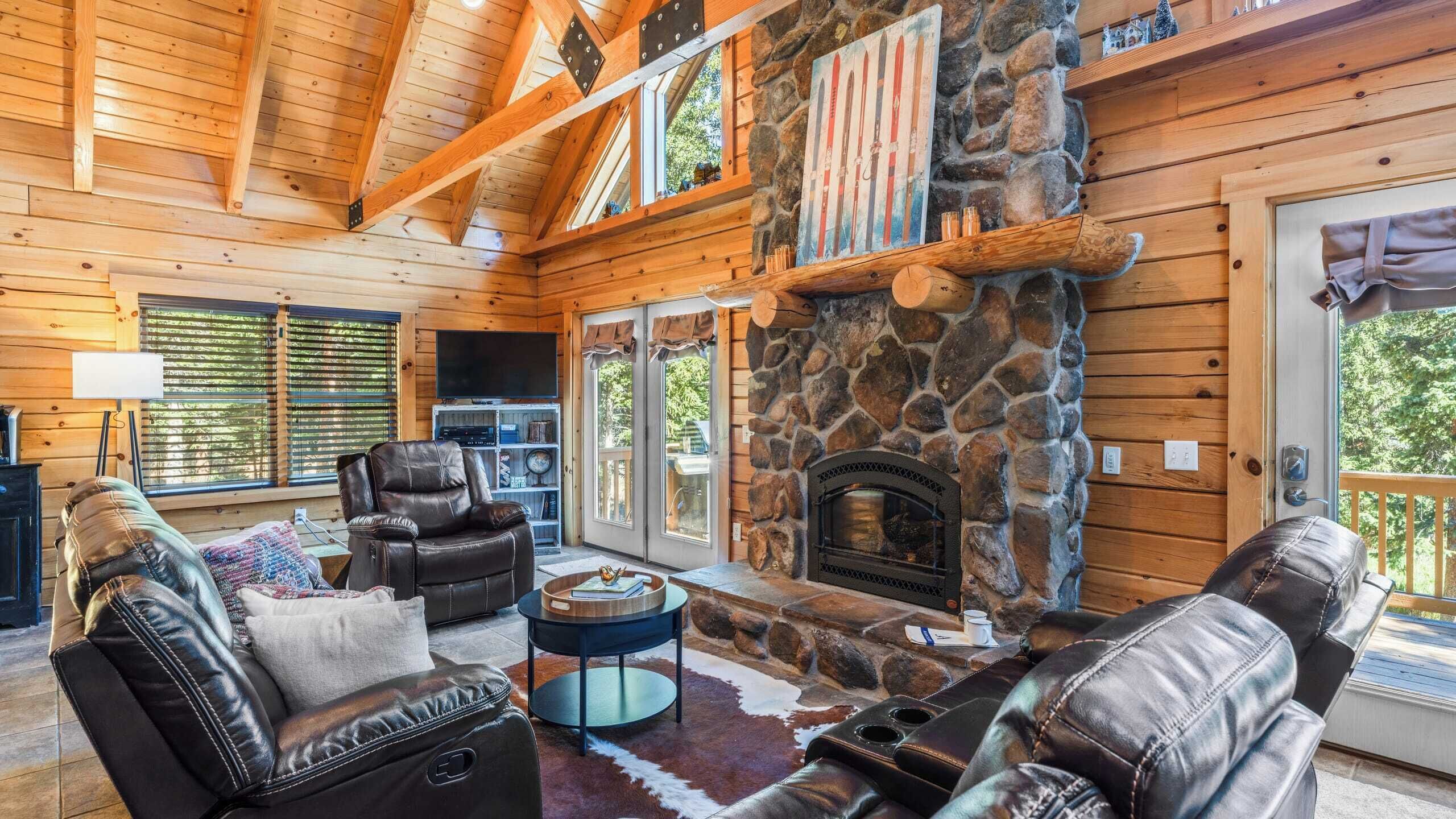 L’intérieur d’un chalet chaleureux, avec une cheminée en pierre, des meubles en cuir et des murs en bois.