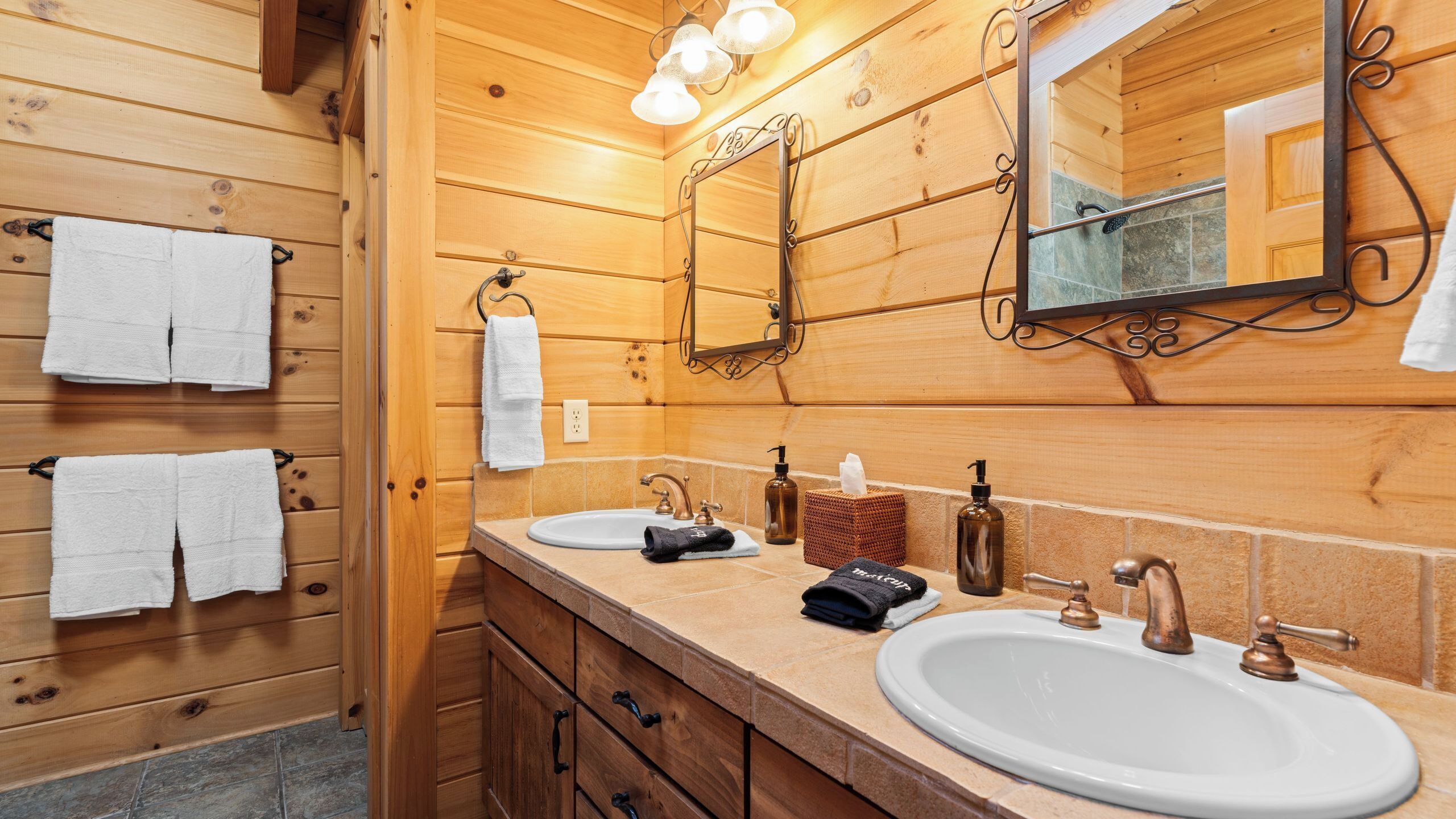Une salle de bain rustique, avec des murs en bois, comprenant deux lavabos, un miroir et des serviettes accrochées à des crochets.