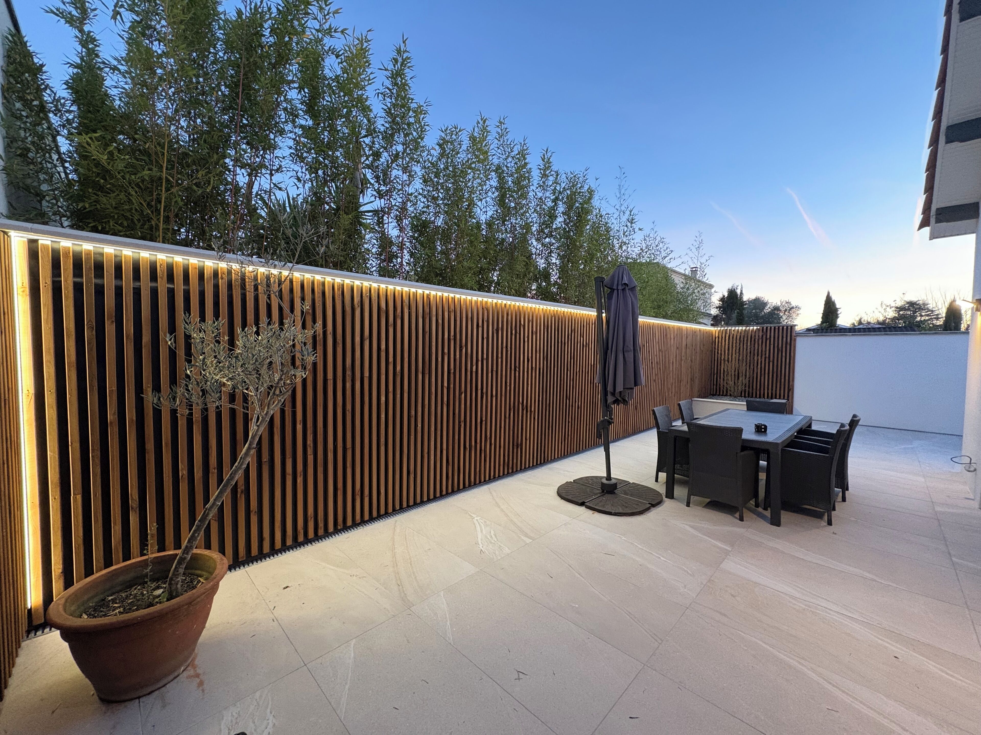Une terrasse extérieure moderne avec un mur en bois à lattes, une table ronde et des chaises.