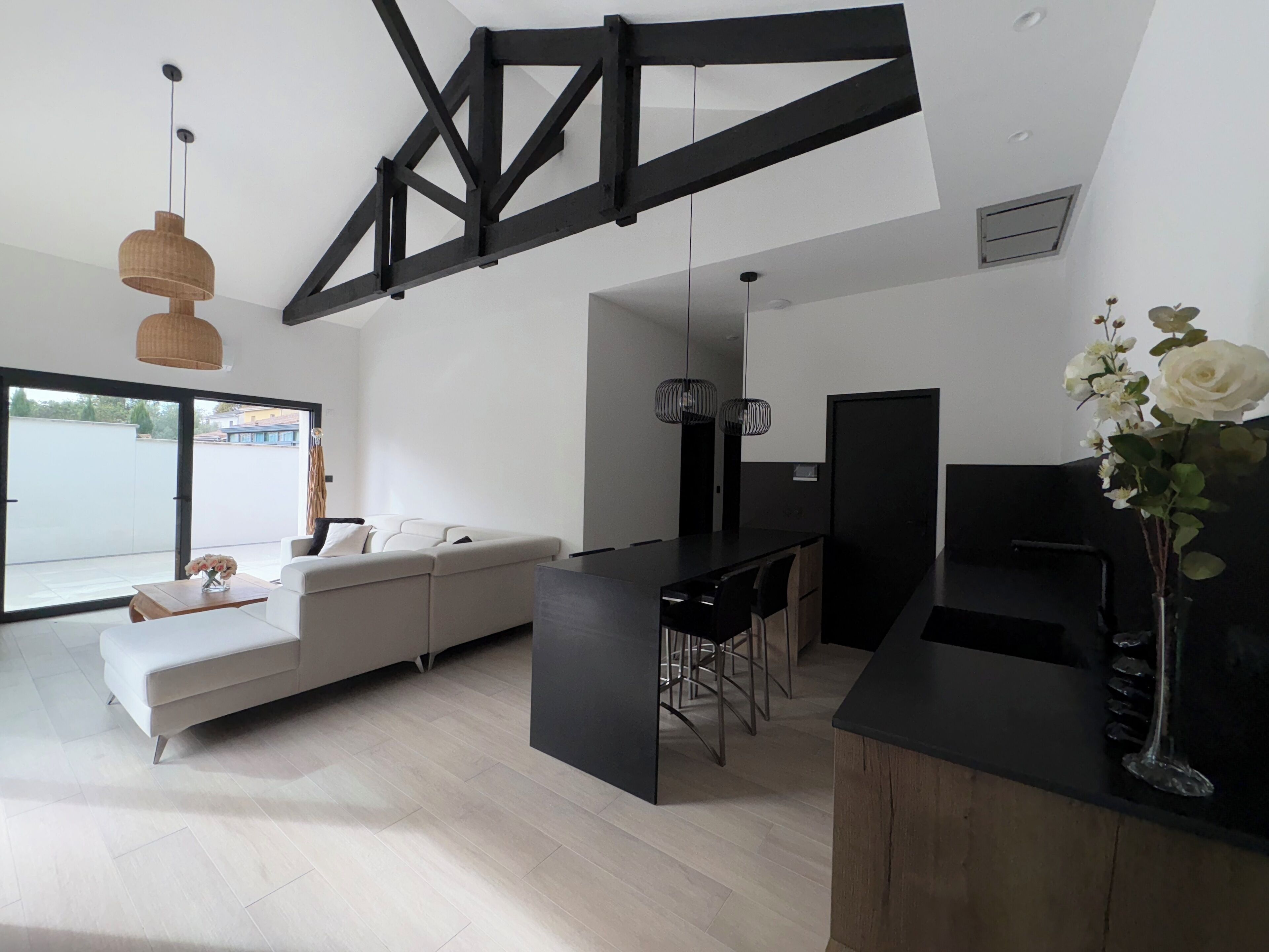 A modern living space with a large white sofa, a dining area with a black table, and a kitchen counter.