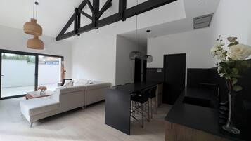 A modern living space with a large white sofa, a dining area with a black table, and a kitchen counter.
