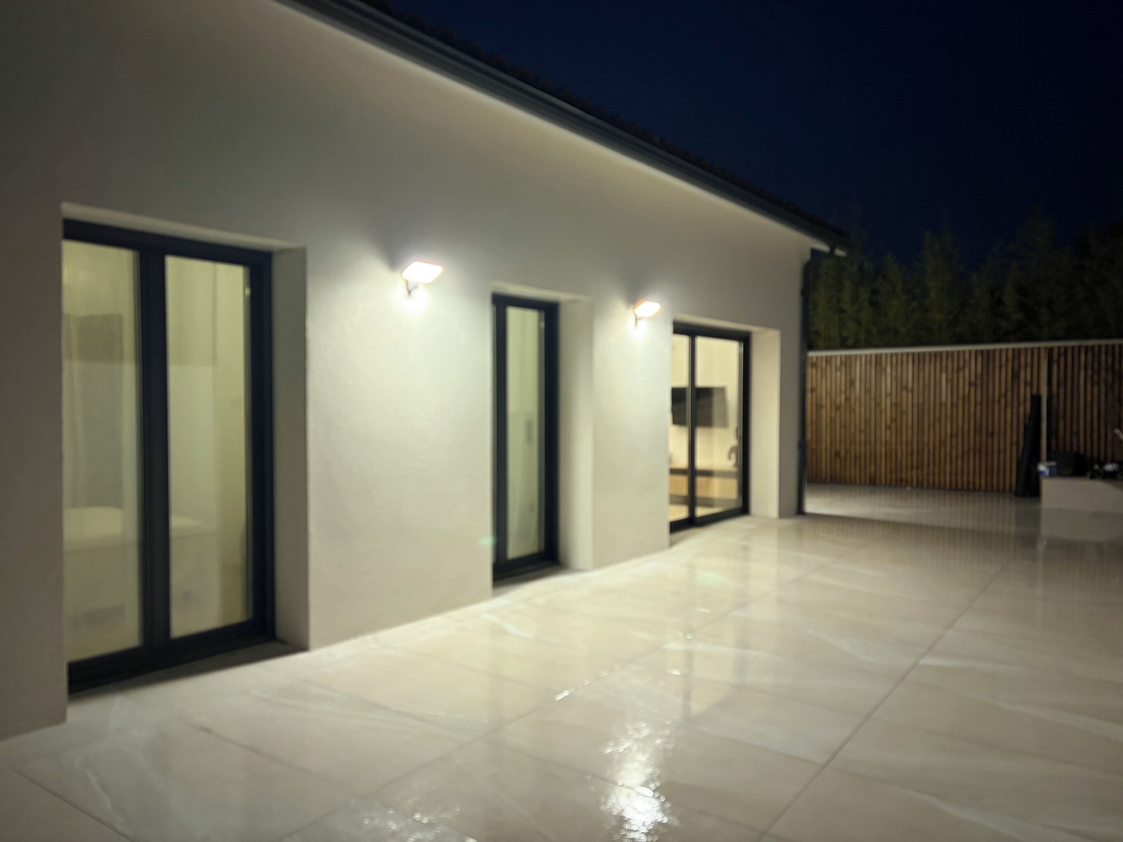 A modern building exterior with large glass doors and windows, a flat roof, and a paved patio area.