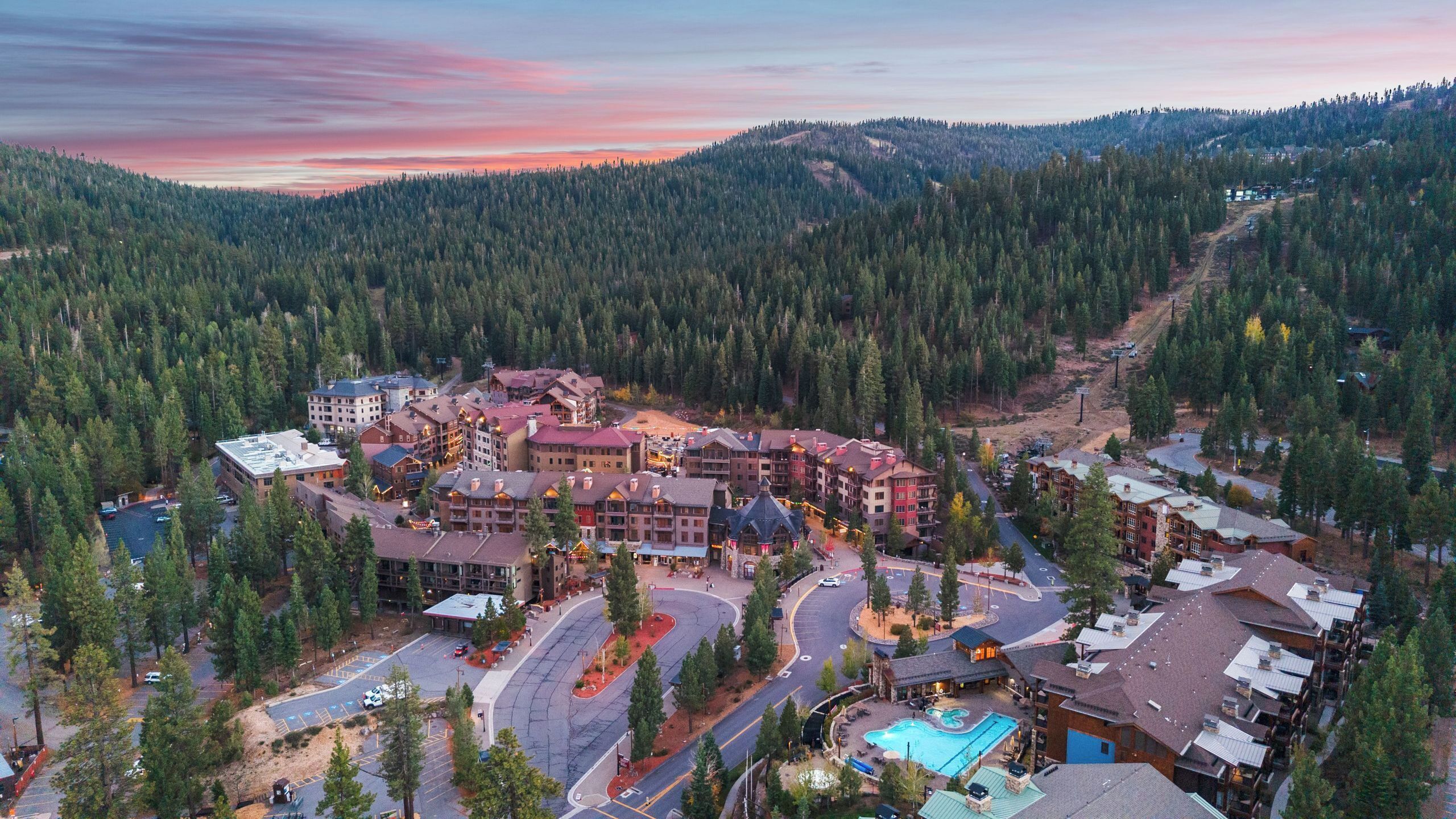 A resort with multiple buildings, a swimming pool, and a mountainous backdrop.