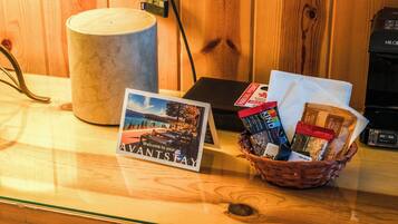 A wooden table with a welcome card, a coffee maker, a basket with snack bars, and a coffee pod.