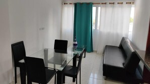 A room with a glass dining table, black chairs, a black sofa, and a teal curtain. - Em3-1g 1 Bedroom Apartment in Residential Area air Conditioning and Wifi (Cartagena)