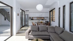 Un salon moderne avec un grand canapé d’angle, une table basse ronde agrémentée d’une plante, et un coin repas avec une table et des chaises à plateau en verre.
