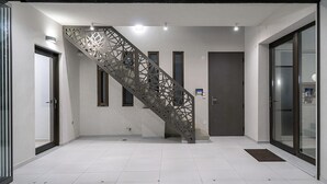 Un intérieur moderne avec un escalier en métal, des carreaux blancs au sol et des portes en verre.