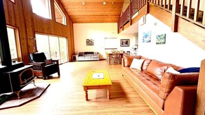 Un amplio salón con suelos de madera, un sofá de cuero marrón, una mesa de centro amarilla y una chimenea.